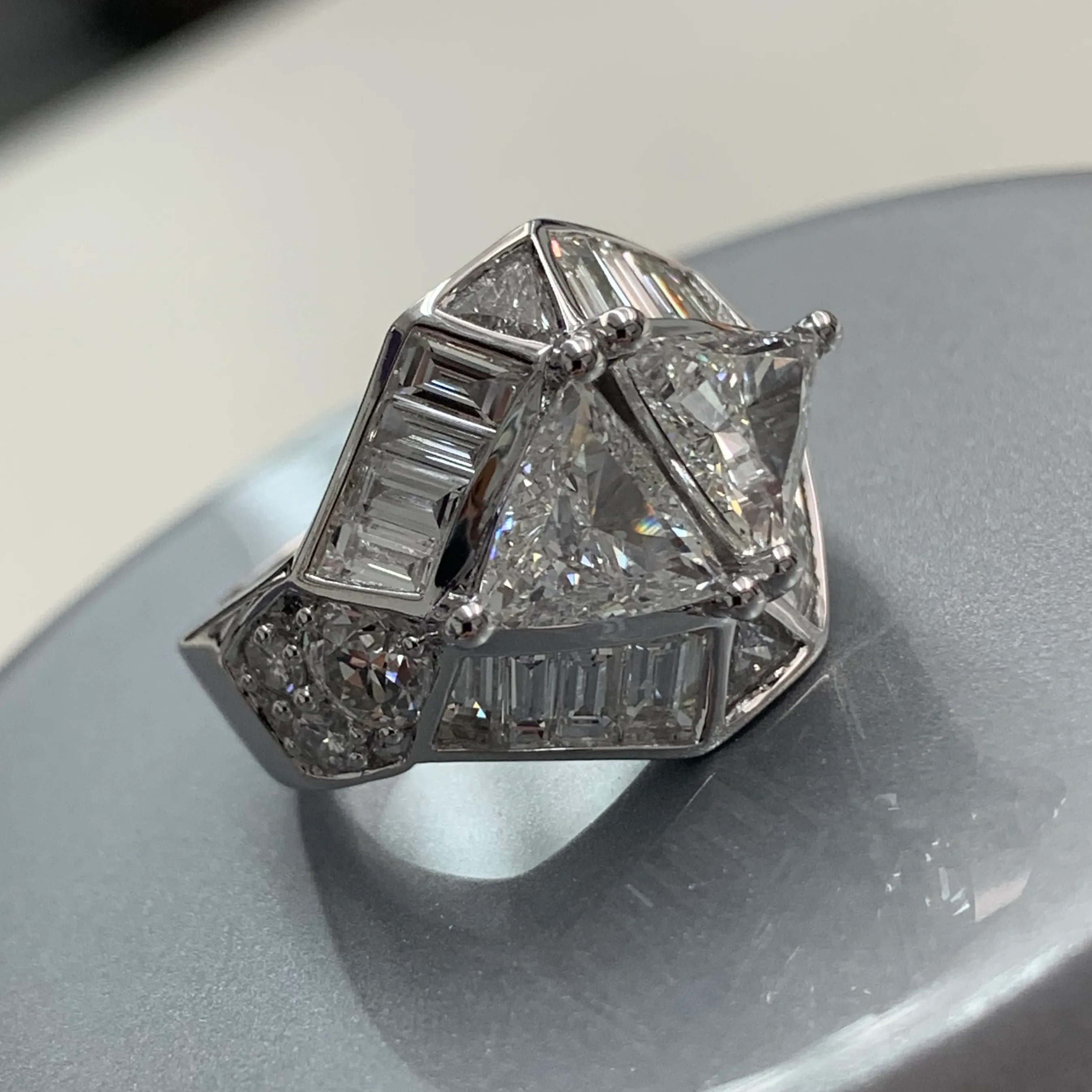 A geometric diamond ring with baguette and round diamonds on a reflective surface.