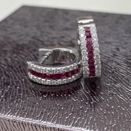 Silver hoop earrings with red and white gemstones on a textured surface.