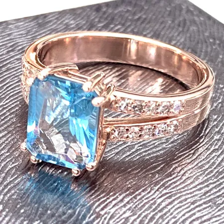 A gold ring with a large blue gemstone and diamond accents on a textured surface.