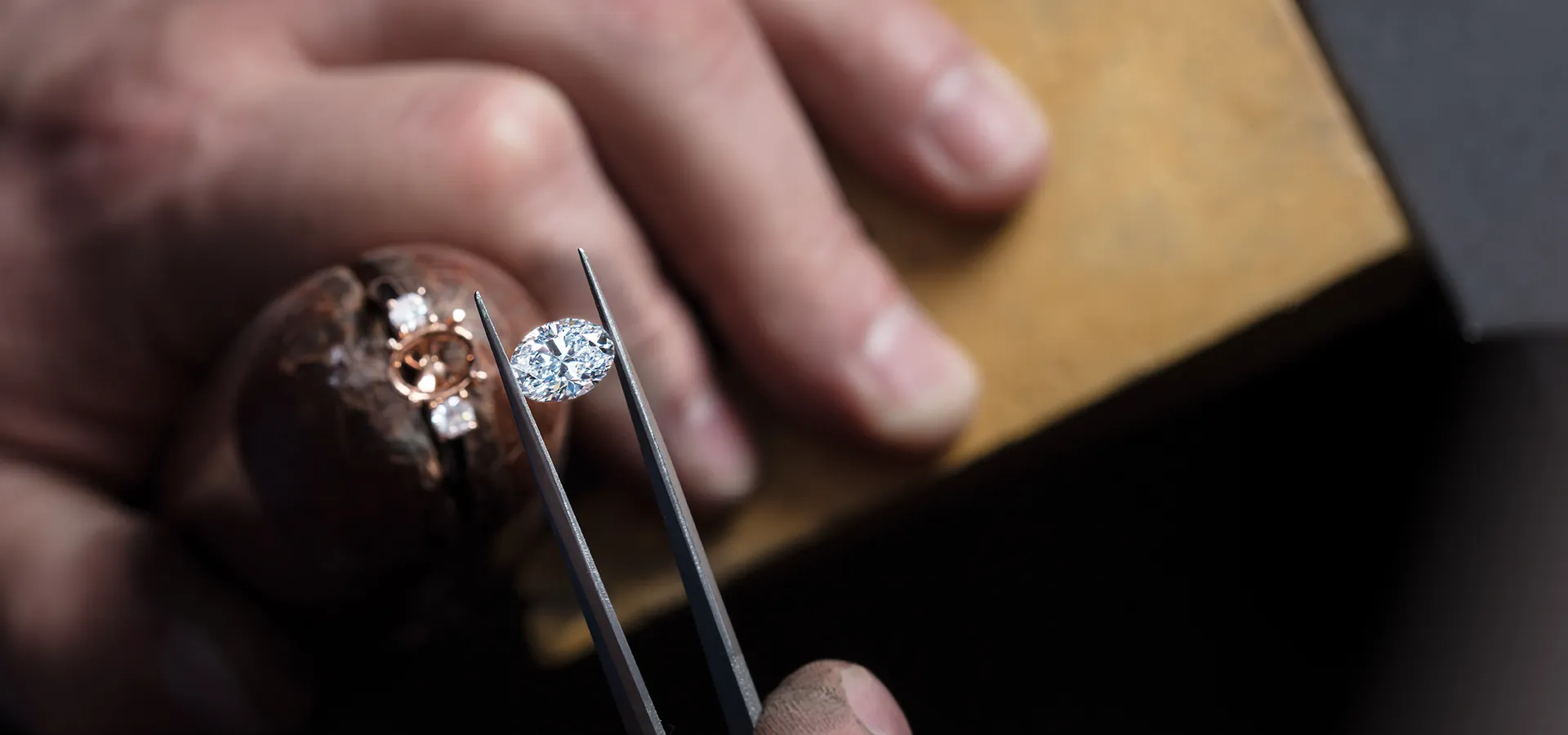 A jeweler holds a diamond with tweezers, preparing to set it in a ring.