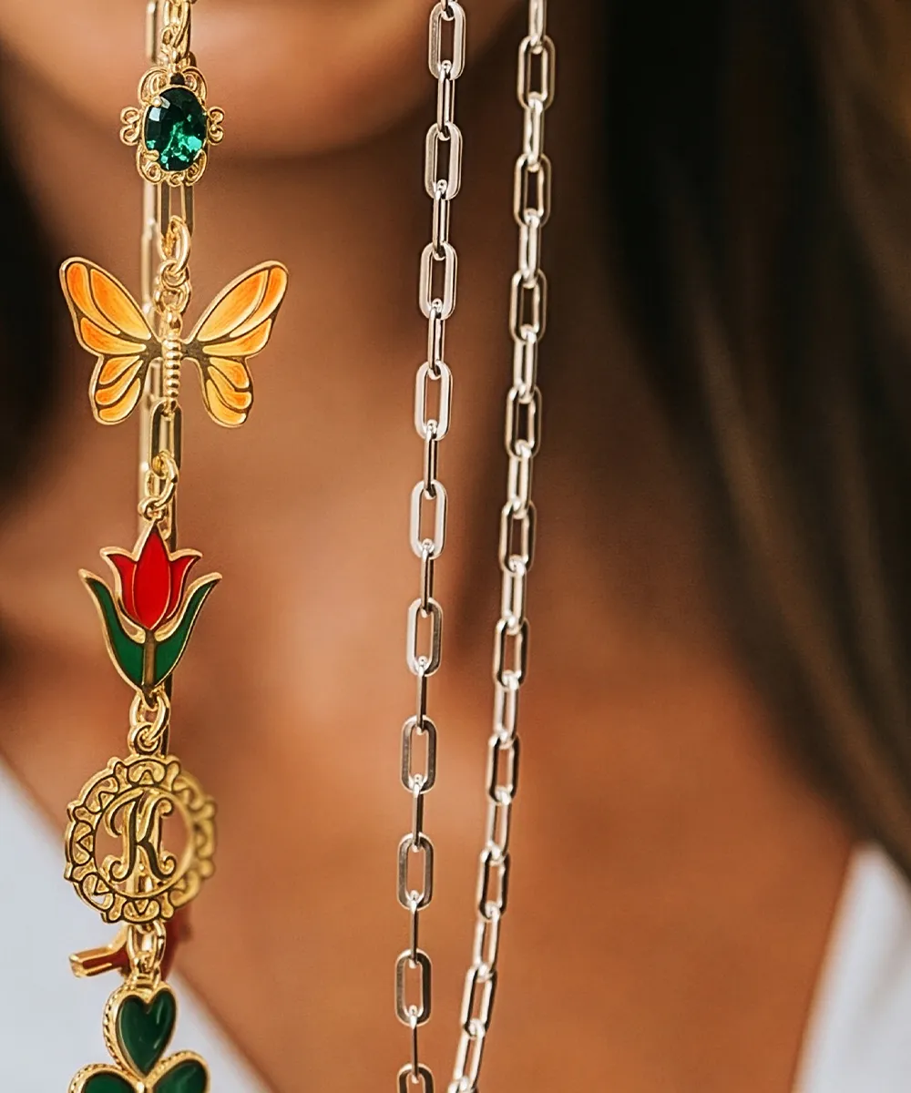 A close-up of gold and silver necklaces with charms, including a butterfly, flower, and letter 