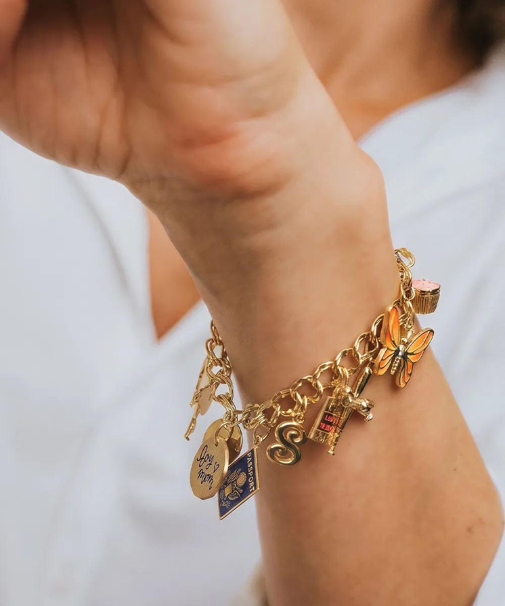 A gold charm bracelet with various charms, including a butterfly, keys, and a heart, on a person's wrist.