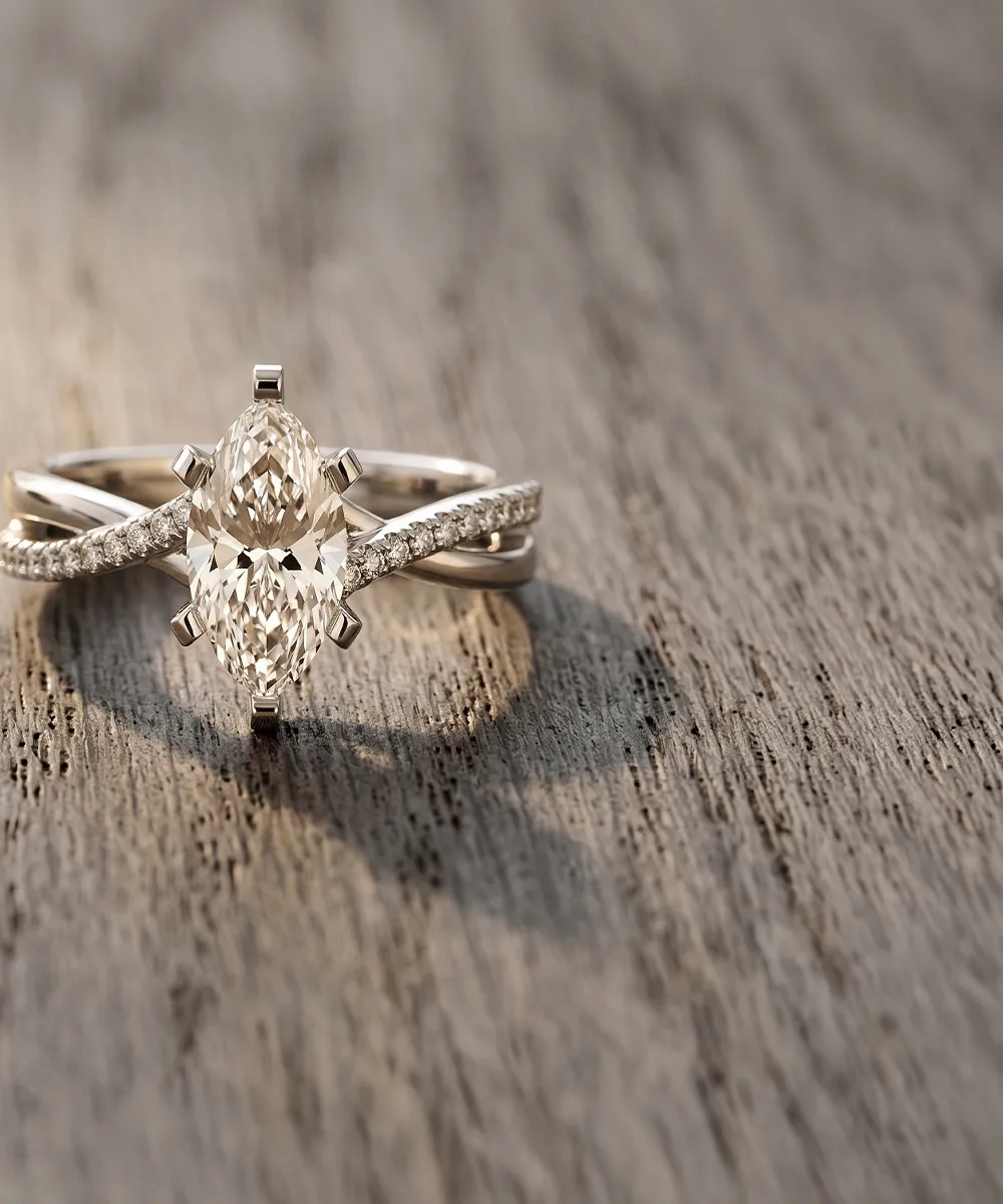 A marquise-cut diamond ring with a twisted band on a wooden surface.
