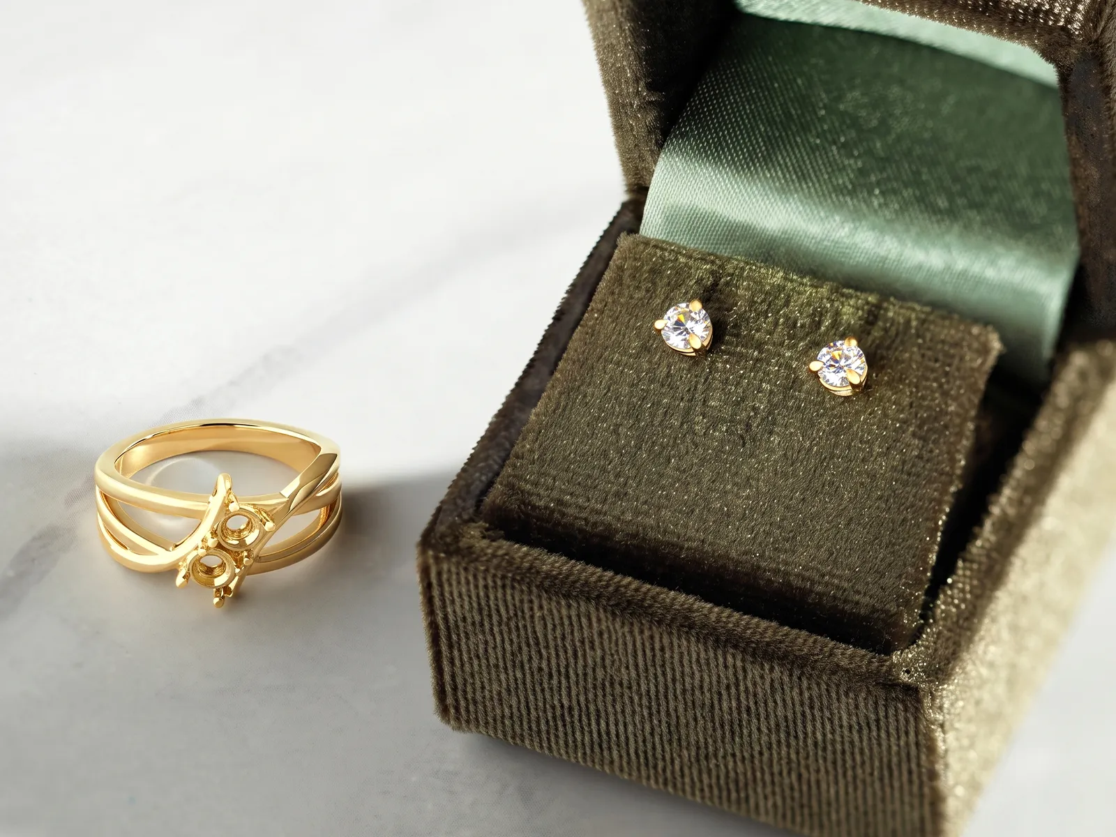 Gold ring and diamond stud earrings in a velvet jewelry box on a marble surface.