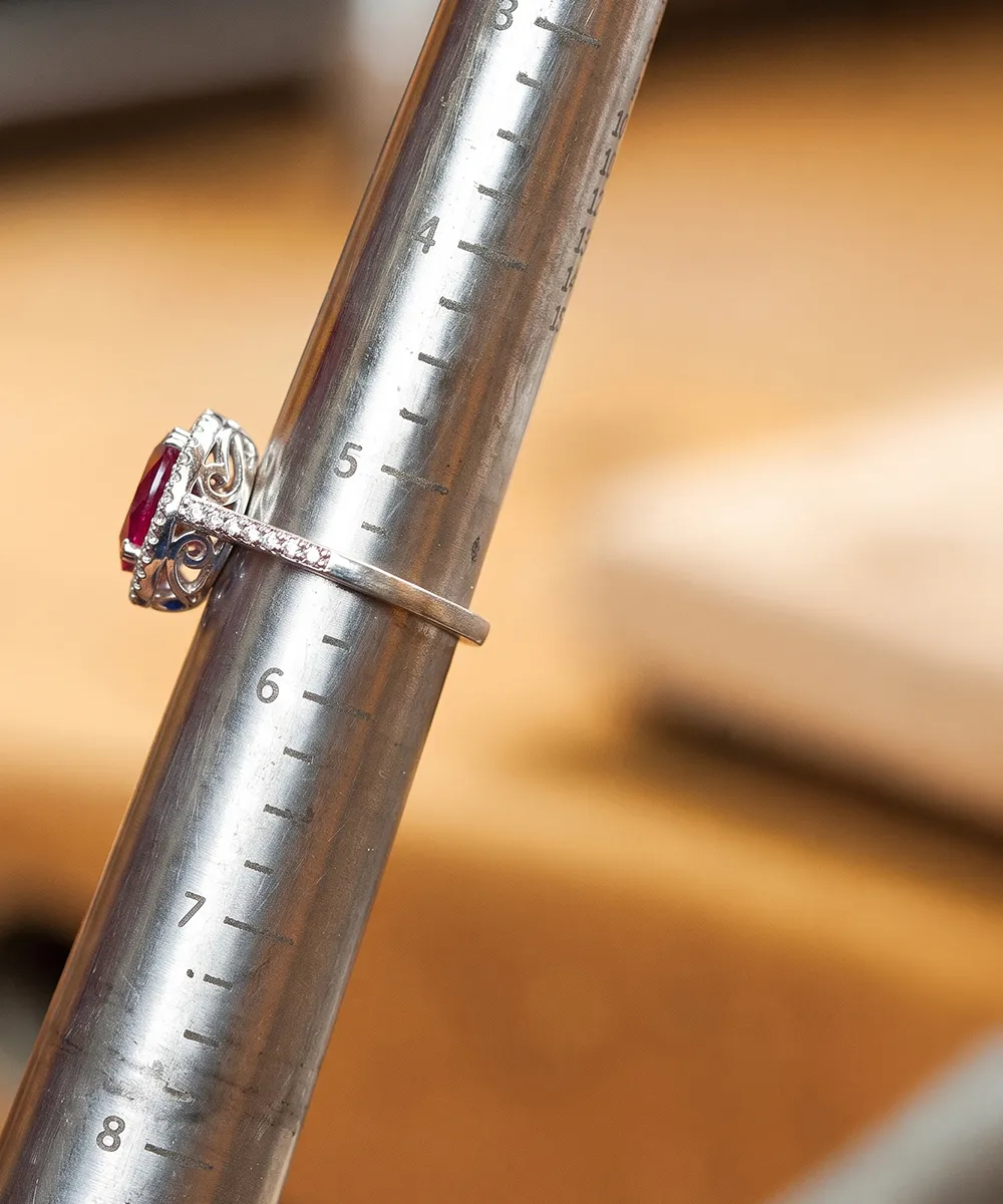 A silver ring with a red gemstone on a metal ring sizer.