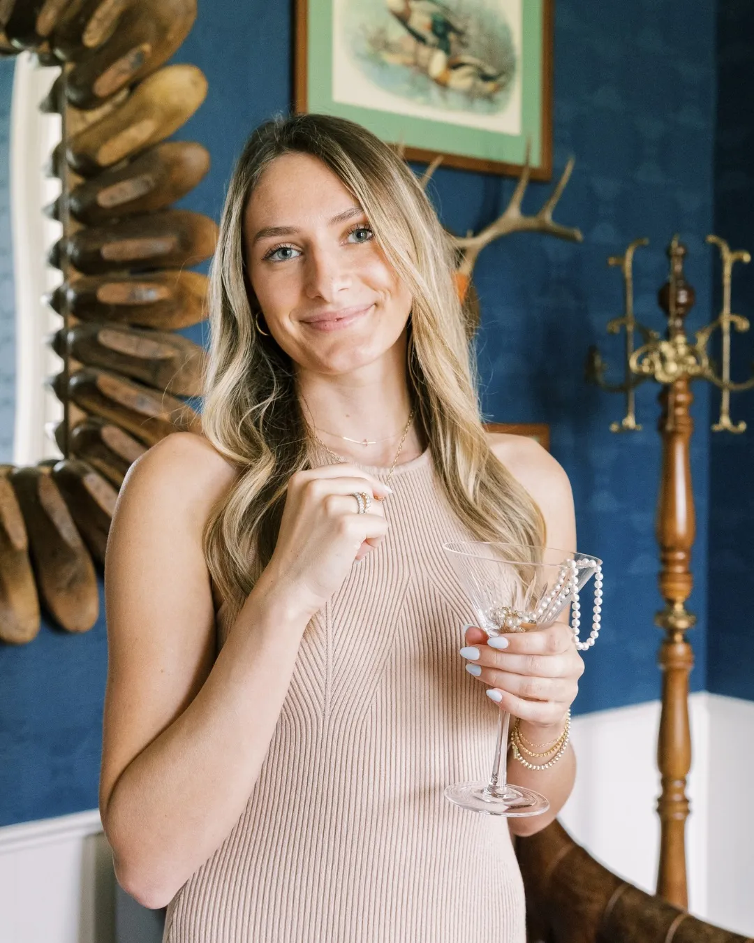 Jaci Spies, owner of Segner's Jewelers, smiles holding a martini glass adorned with pearls in a stylish setting.