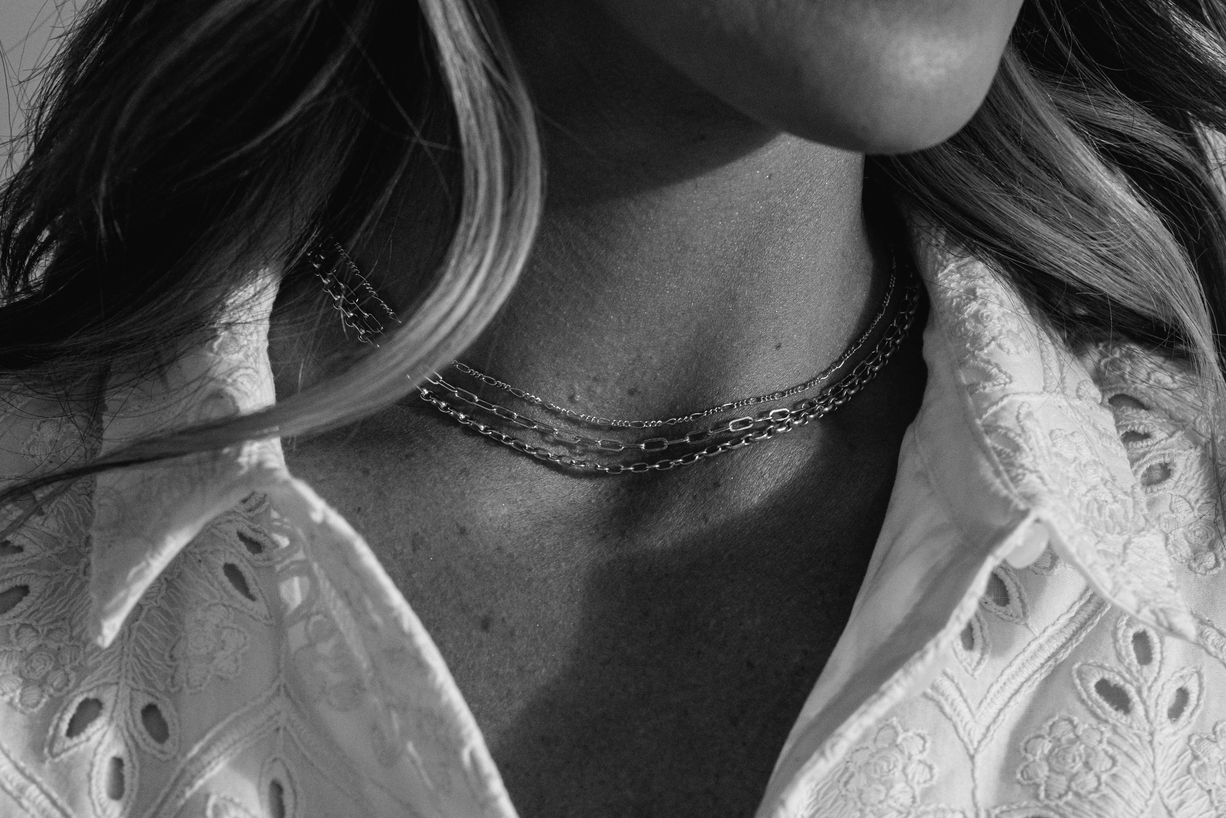 Close-up of layered silver chains worn on a woman's neck, showcasing elegant jewelry style. Explore more at Segner's Jewelers.
