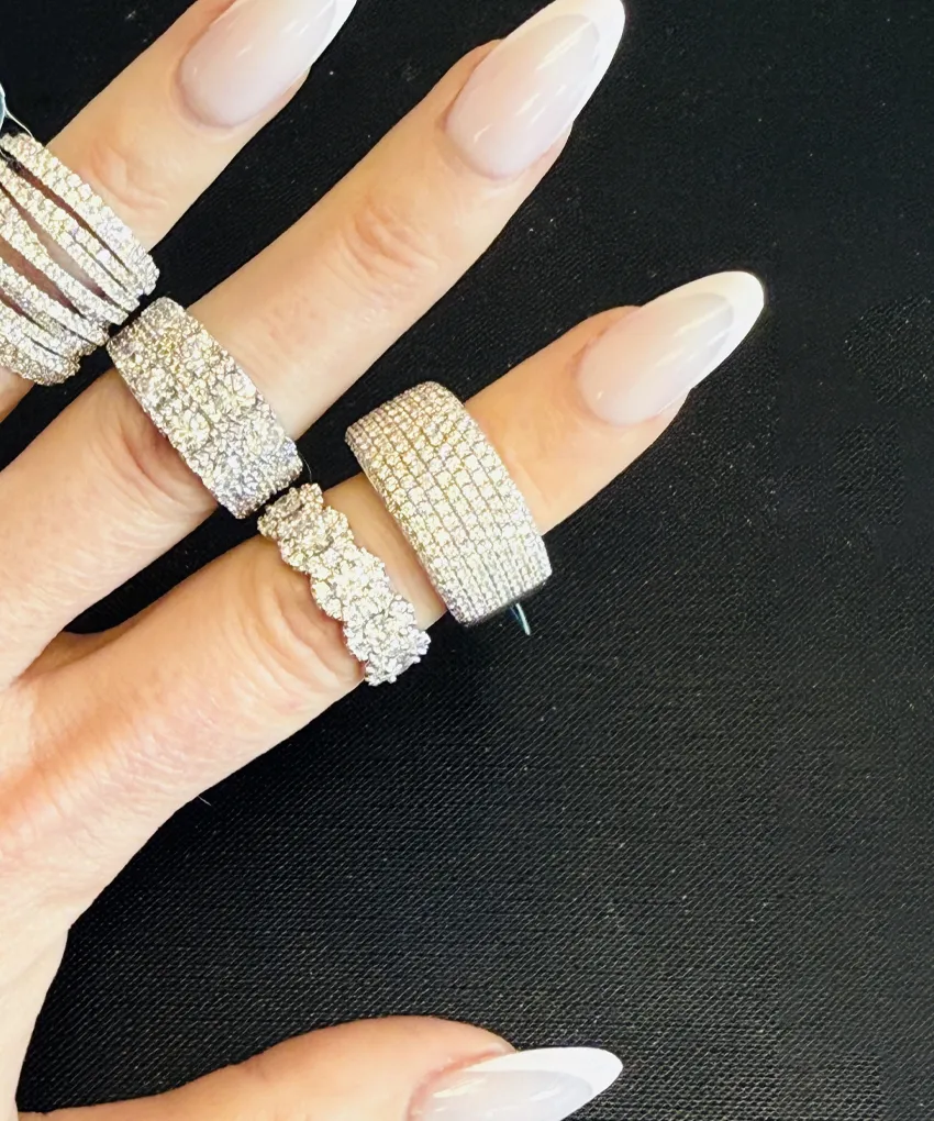 Hand with manicured nails wearing multiple sparkling diamond rings on black background.