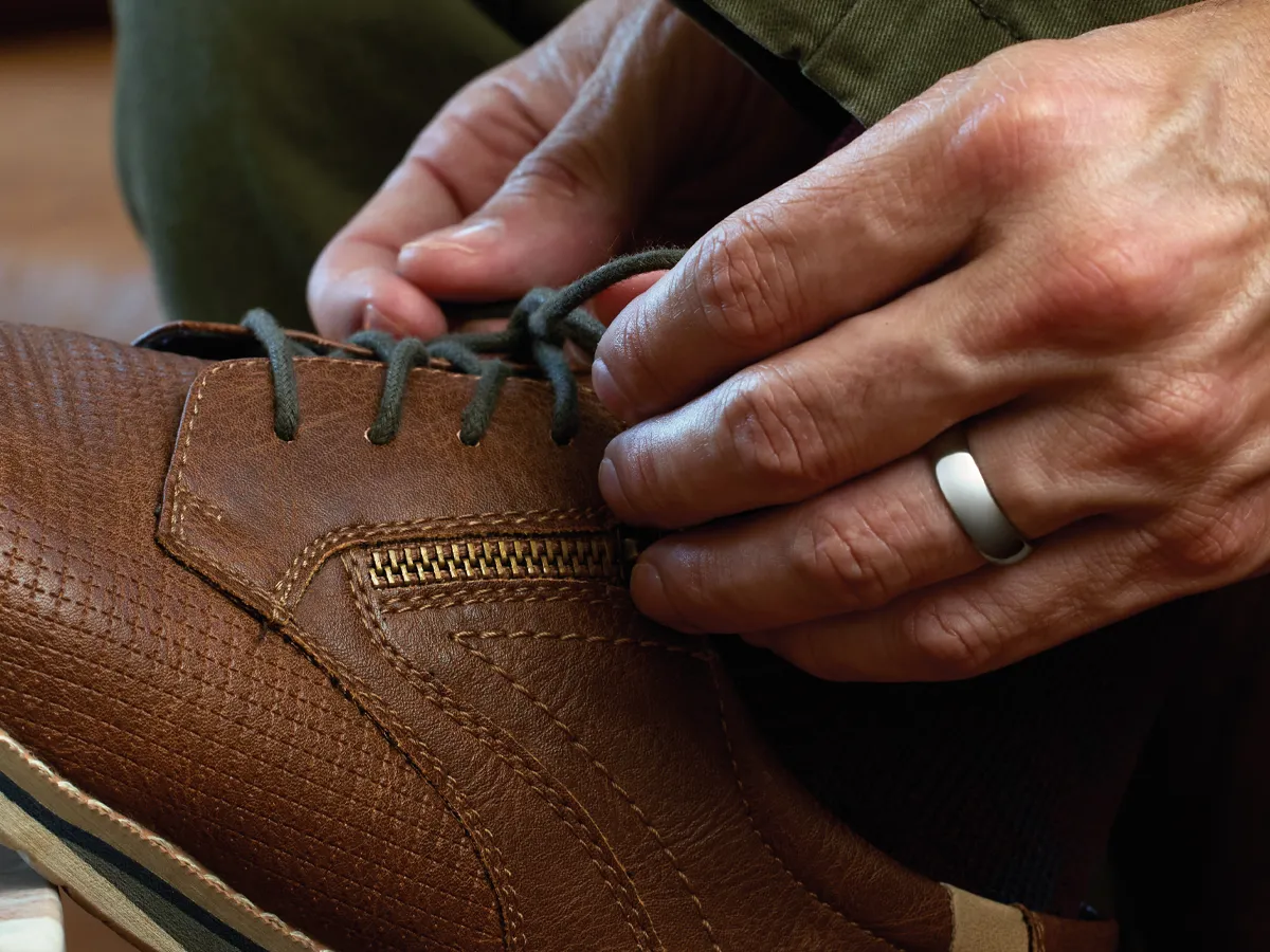 Hands tying laces on a brown leather shoe with a zipper detail.