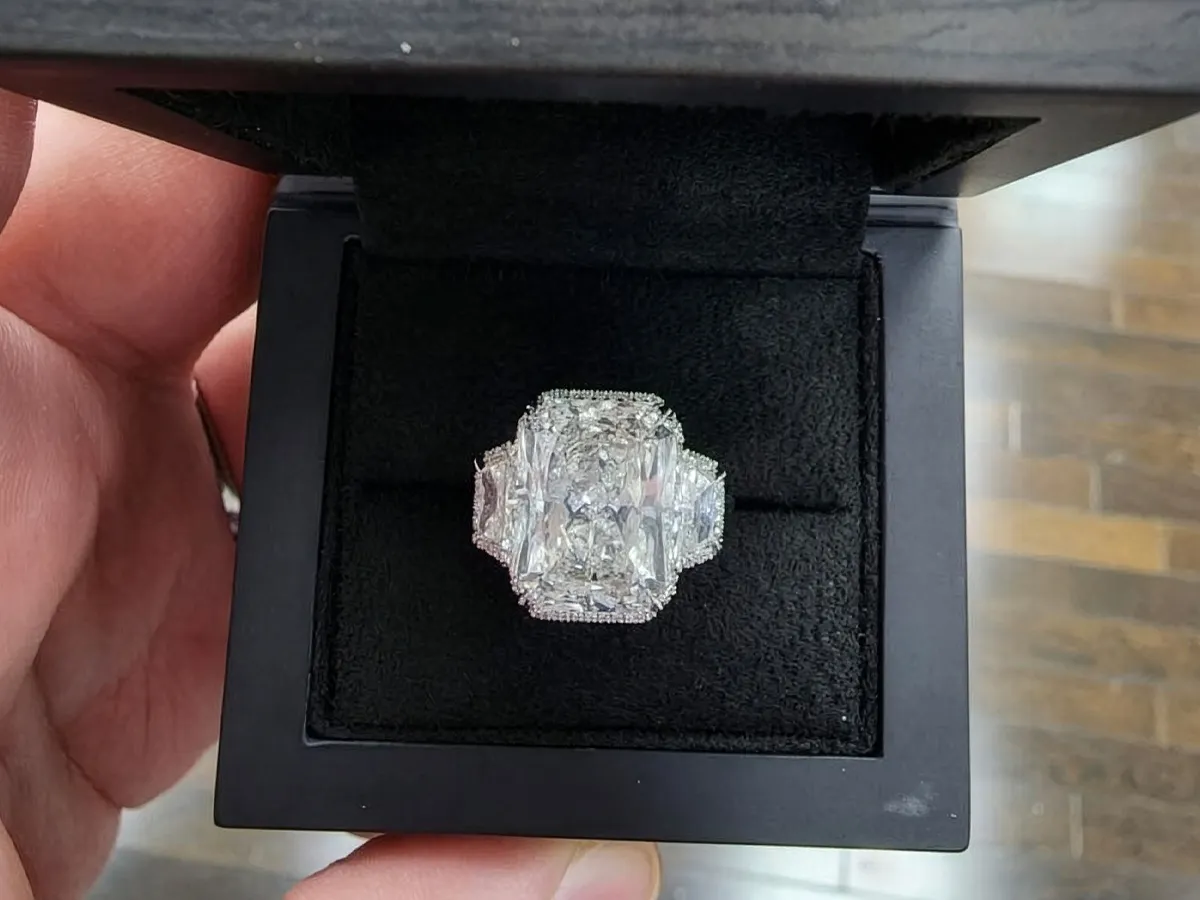 A large diamond ring in a black jewelry box, held by a hand.