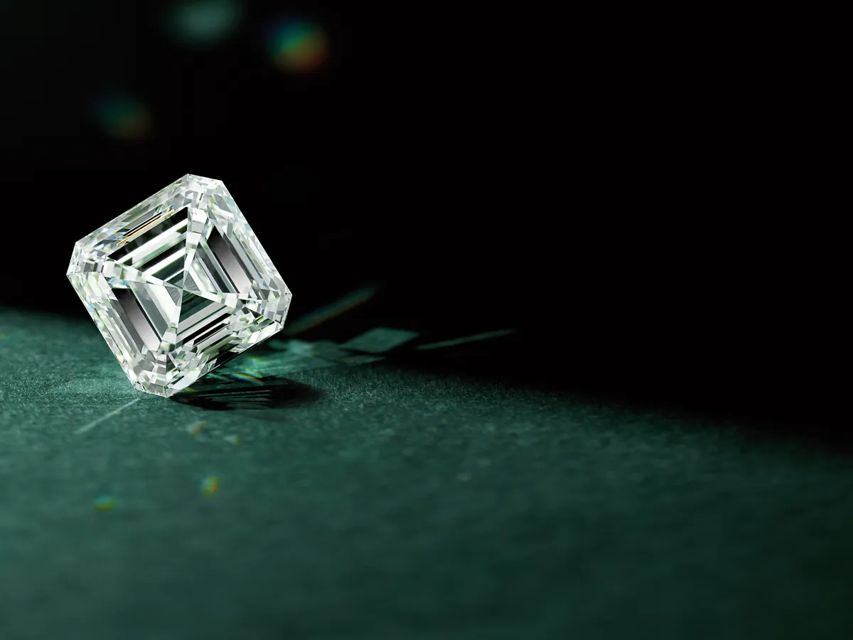 A radiant-cut diamond on a dark surface with light reflections.