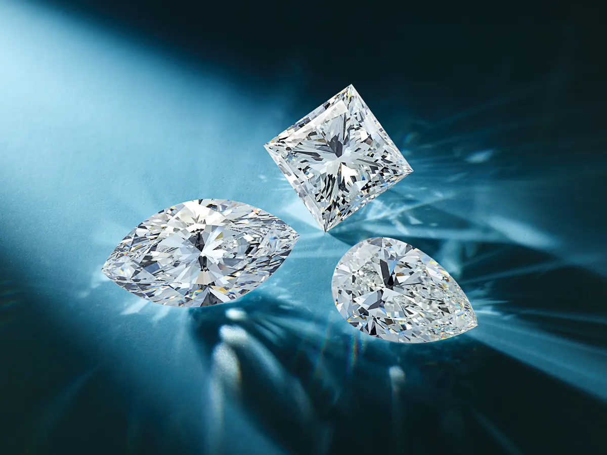 Three sparkling diamonds in marquise, princess, and pear cuts on a blue background.