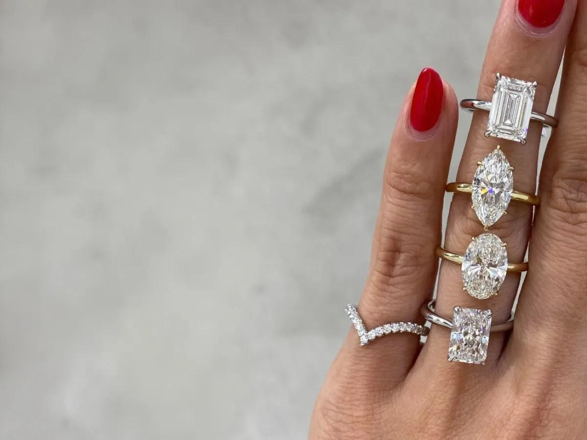 Hand with red nails displaying four diamond rings on fingers.