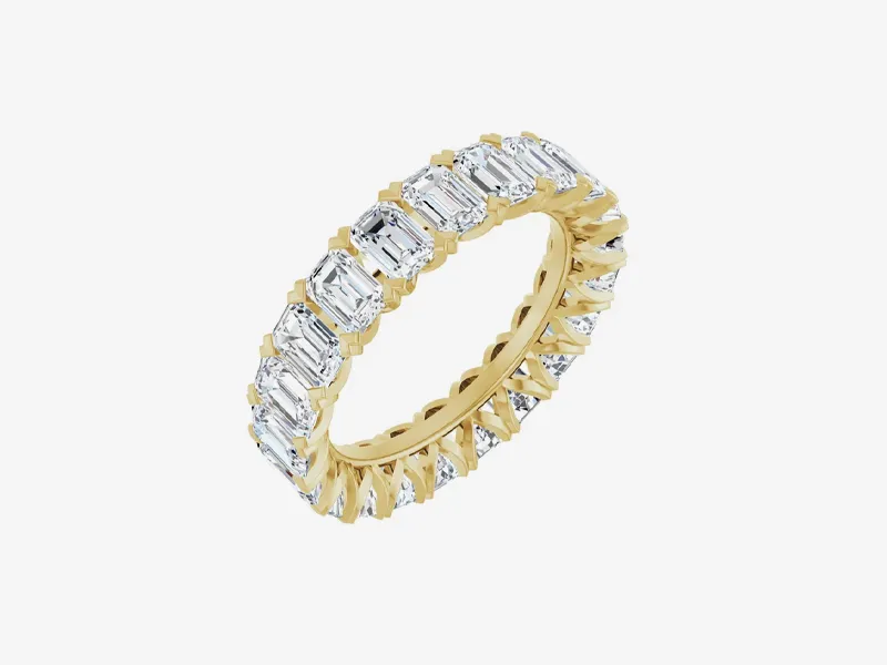 Gold eternity band with emerald-cut diamonds, displayed on a white background.