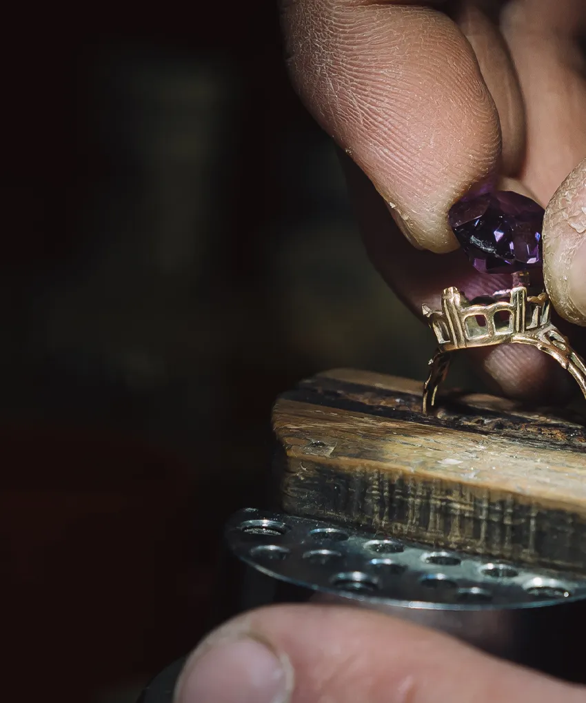 Craftsman setting a purple gemstone into a gold ring on a workbench.