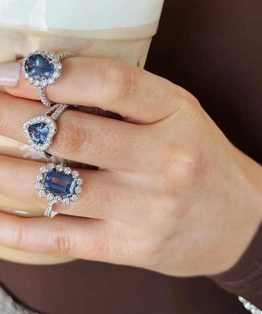 Hand holding a coffee cup, adorned with three blue gemstone rings.