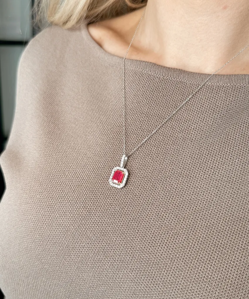 A woman wearing a silver necklace with a red gemstone pendant over a beige sweater.