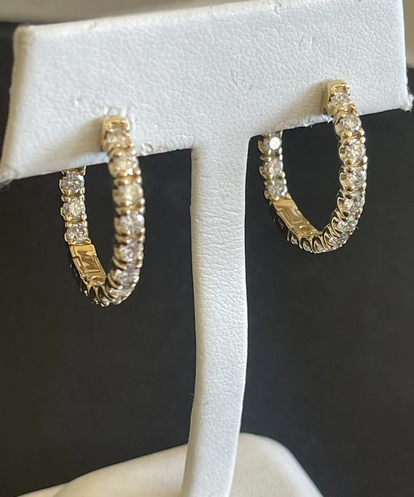 Gold hoop earrings with diamonds displayed on a white stand.