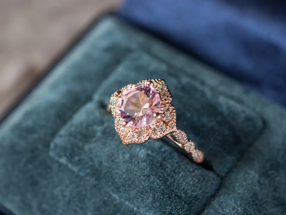 Elegant rose gold ring with a pink gemstone and diamond accents on a blue velvet box.