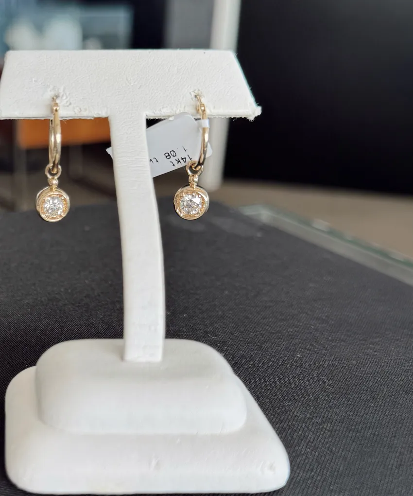 Gold hoop earrings with dangling round diamonds on a white display stand.