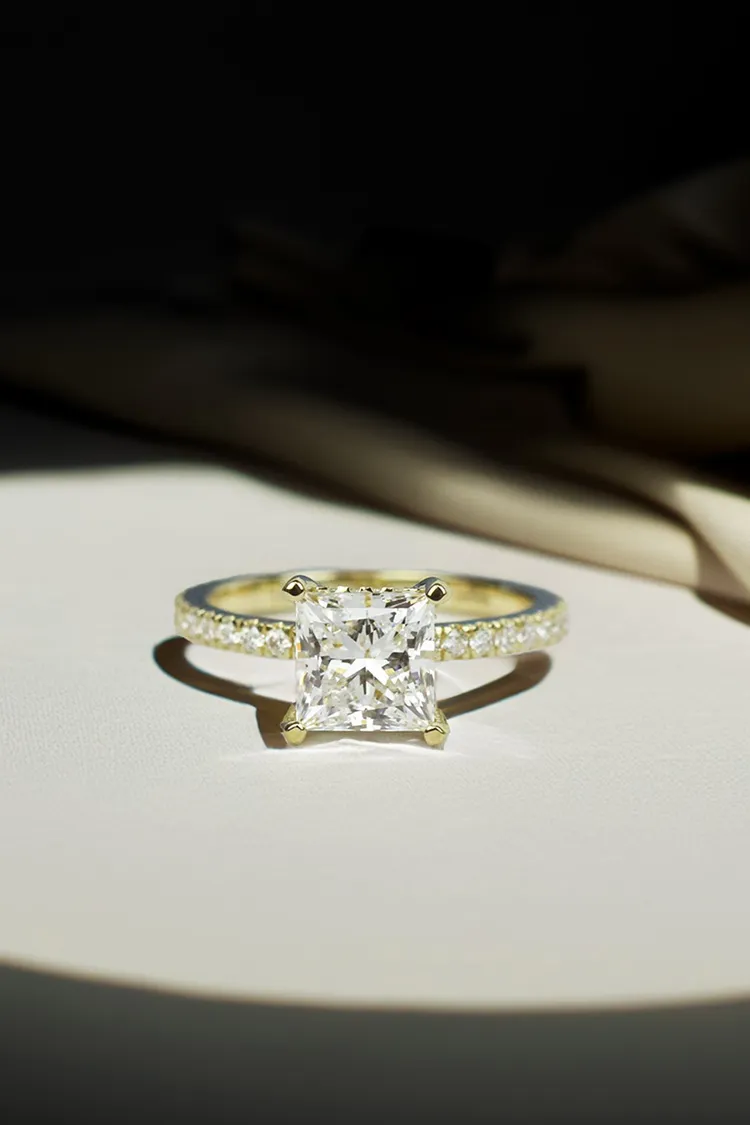 Elegant diamond engagement ring with a square cut stone and sparkling band, displayed on a soft surface.