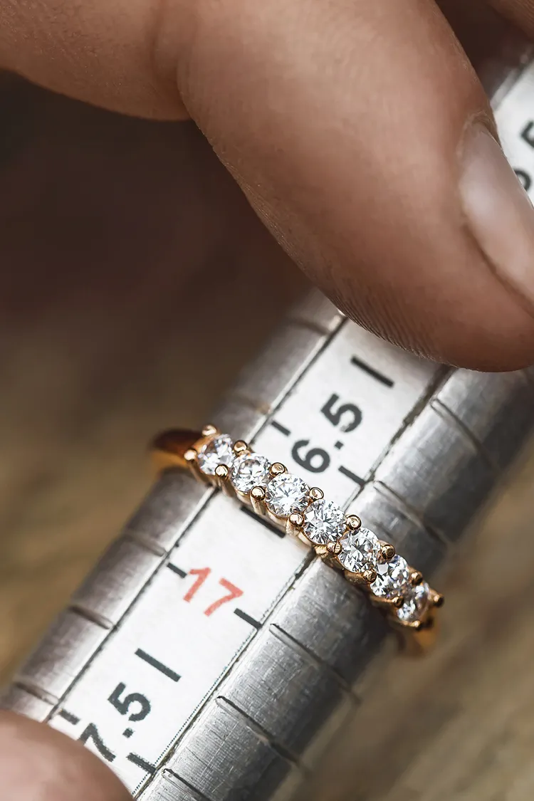 A hand holding a diamond ring on a ring sizer, measuring size 17.