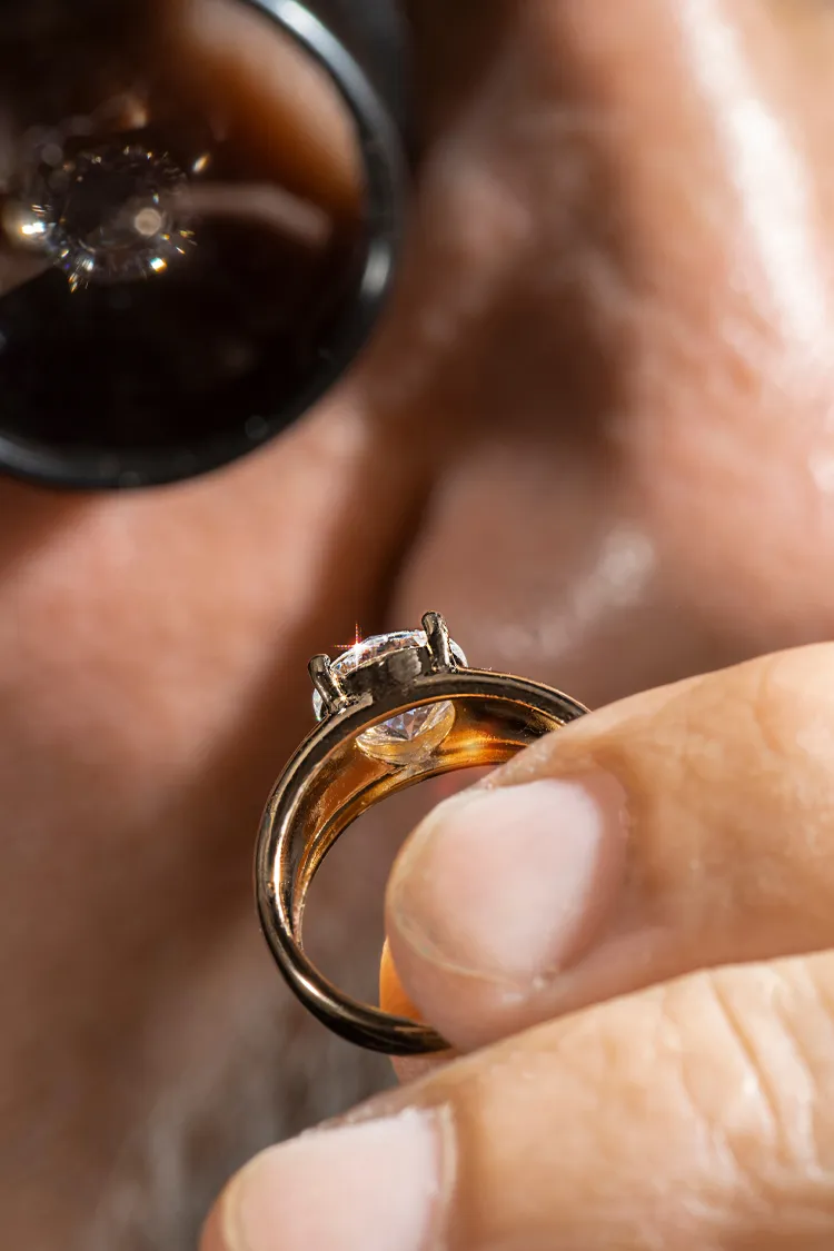 A jeweler inspects a diamond ring closely, highlighting its intricate details and craftsmanship.