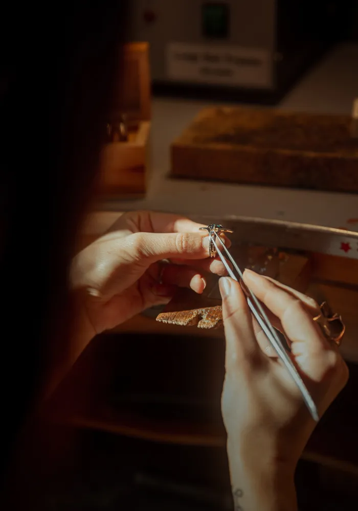 Jeweler crafting a custom ring with tweezers, showcasing intricate details in a workshop setting.