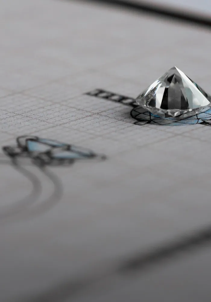 A diamond sits atop a design sketch for jewelry, showcasing the custom design process.