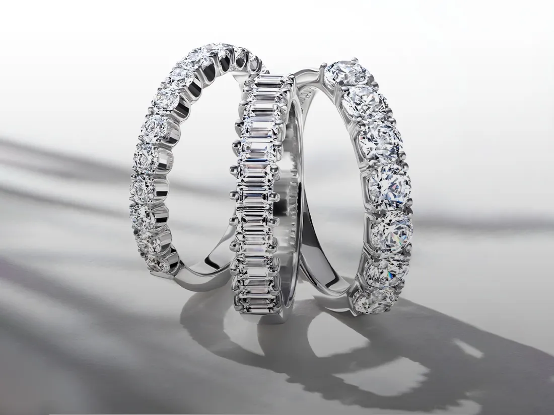 Three elegant diamond rings featuring round and emerald-cut stones, displayed on a reflective surface.