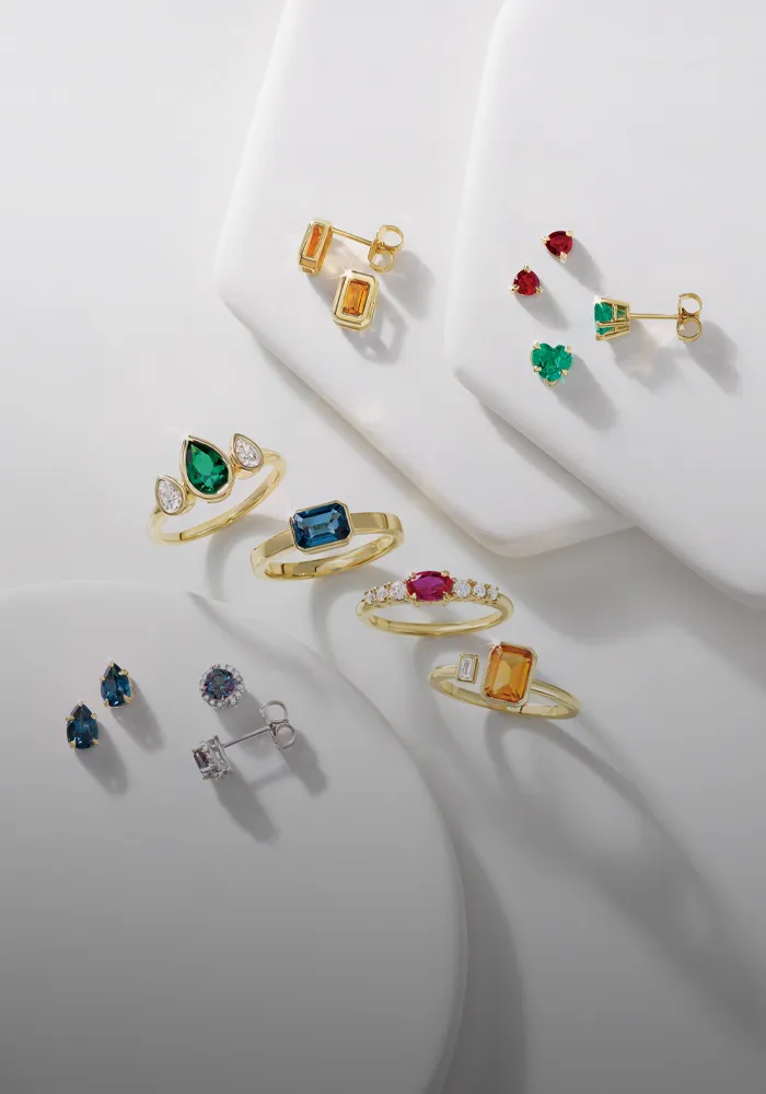Colorful gemstone rings and earrings in gold settings, featuring various stones like emerald, ruby, and sapphire. 
