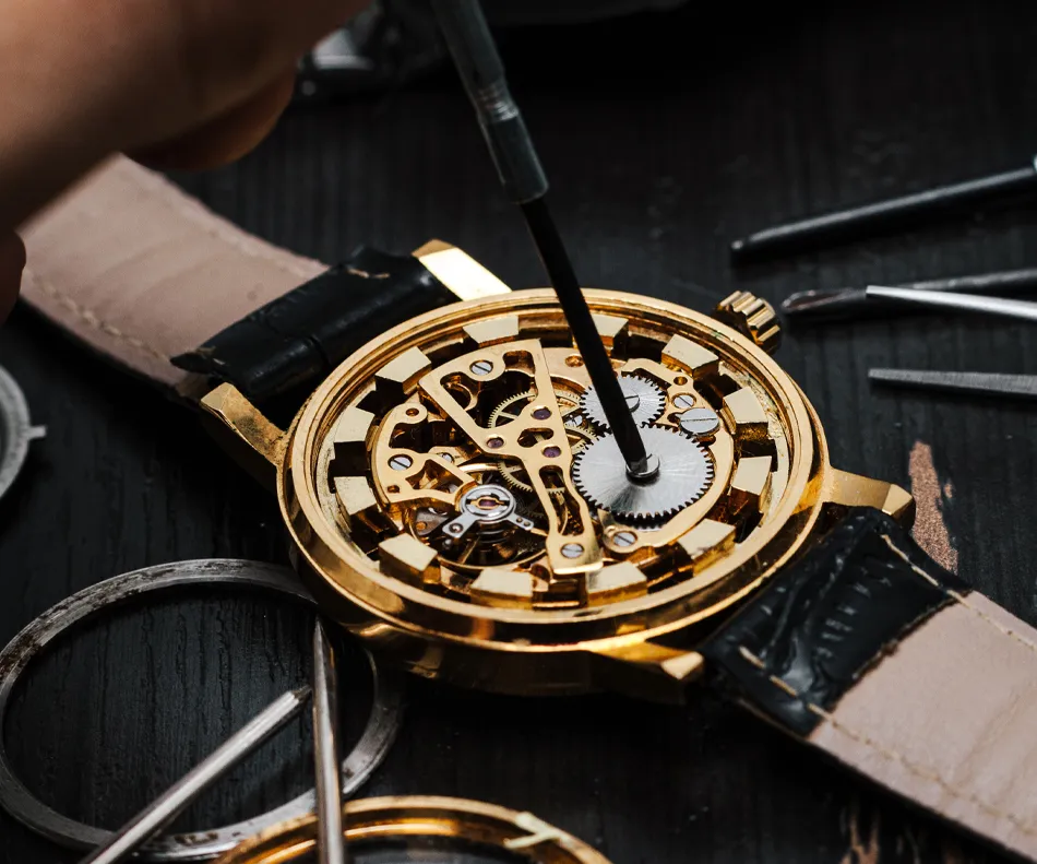 A close-up of a gold watch being repaired, showcasing intricate gears and tools on a dark surface.