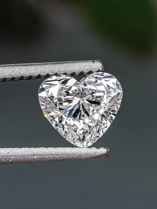 Heart-shaped diamond held by tweezers, showcasing its brilliance and clarity.