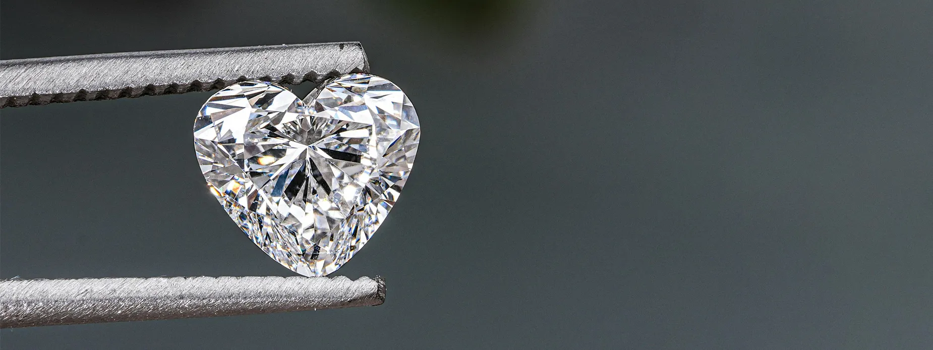 Heart-shaped diamond held by tweezers, showcasing its brilliance and clarity.