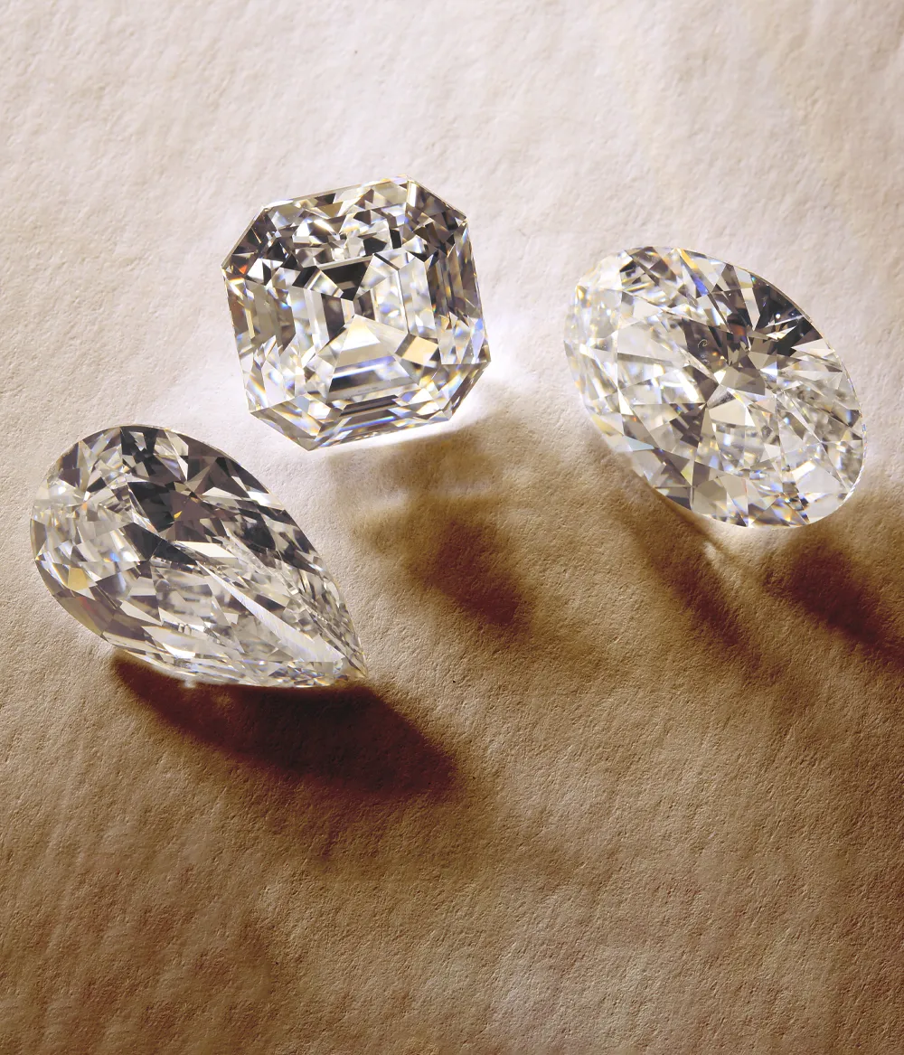 Three sparkling diamonds in various cuts on a textured surface, showcasing their brilliance and clarity.
