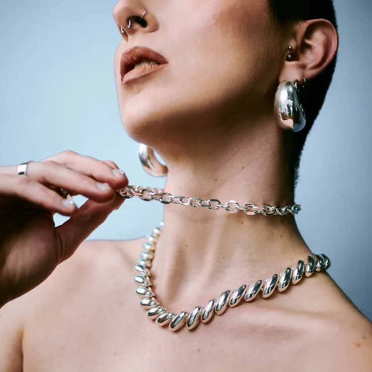 Model showcasing sculptural silver jewelry against a blue background. Click to shop at Simones Jewelry.