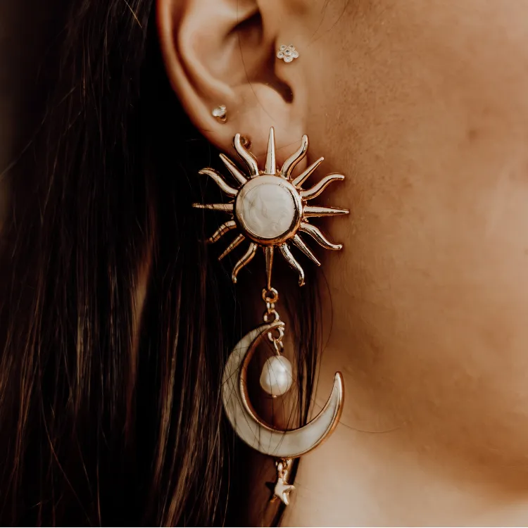 Sun and moon-themed earrings with pearl detail on a woman's ear. Click to Shop Now at Simones Jewelry.
