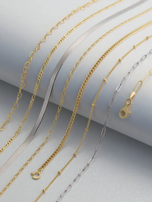 Various gold and silver chains displayed on a light background, showcasing anklet options from Simones Jewelry, LLC.