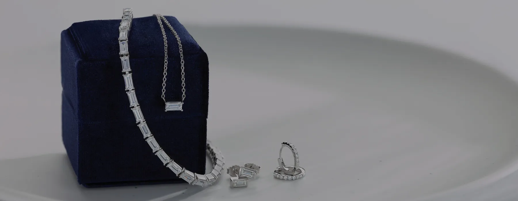 Elegant silver jewelry set including a necklace, earrings, and bracelet displayed on a blue velvet box. Click to shop all jewelr