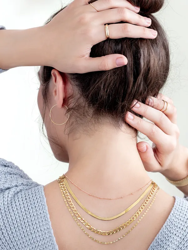 Woman with a bun wearing layered gold chains and earrings, showcasing jewelry from Simones Jewelry, LLC. Click to explore!