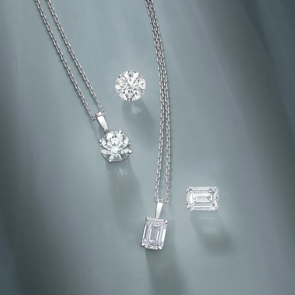 Elegant diamond jewelry featuring a round pendant and emerald-cut stones on a soft gray background.