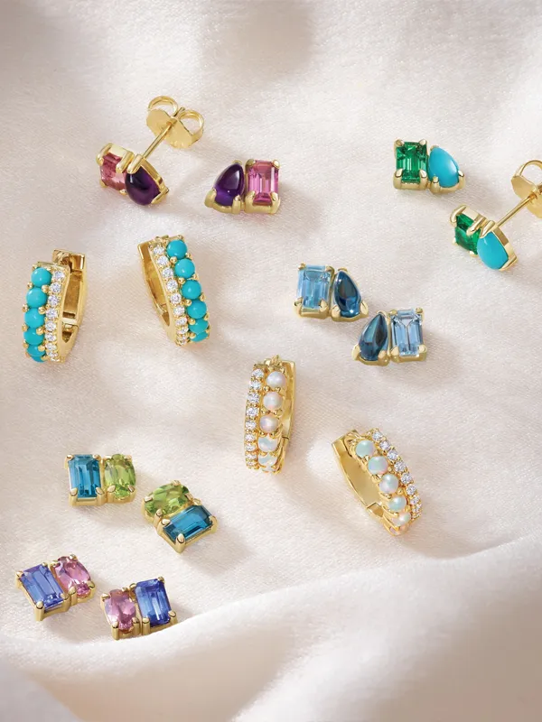Colorful earrings displayed on soft fabric, featuring gold accents and various gemstones. Click to explore more at Simones Jewel