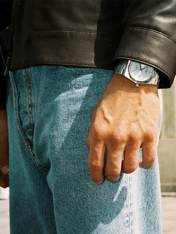 Close-up of a man's hand wearing a silver watch, with denim jeans and a leather jacket. Click to explore watches at Simones Jewe