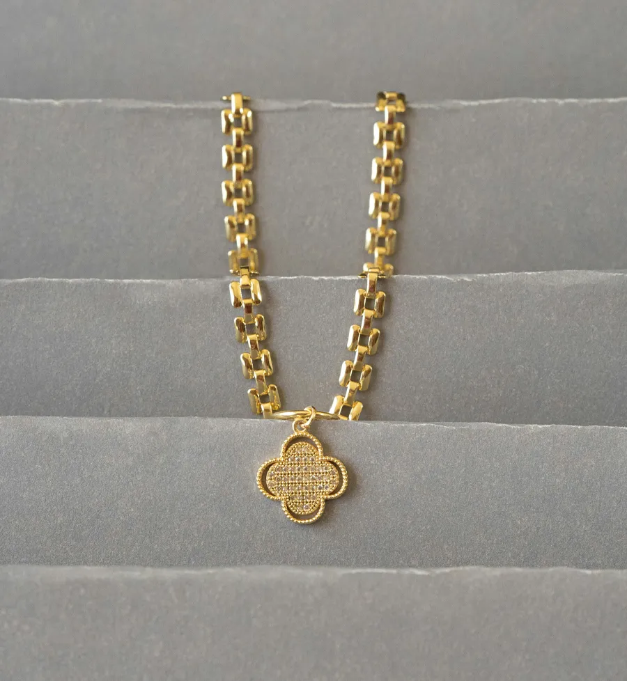 Gold chain necklace with a clover pendant displayed on a soft background.