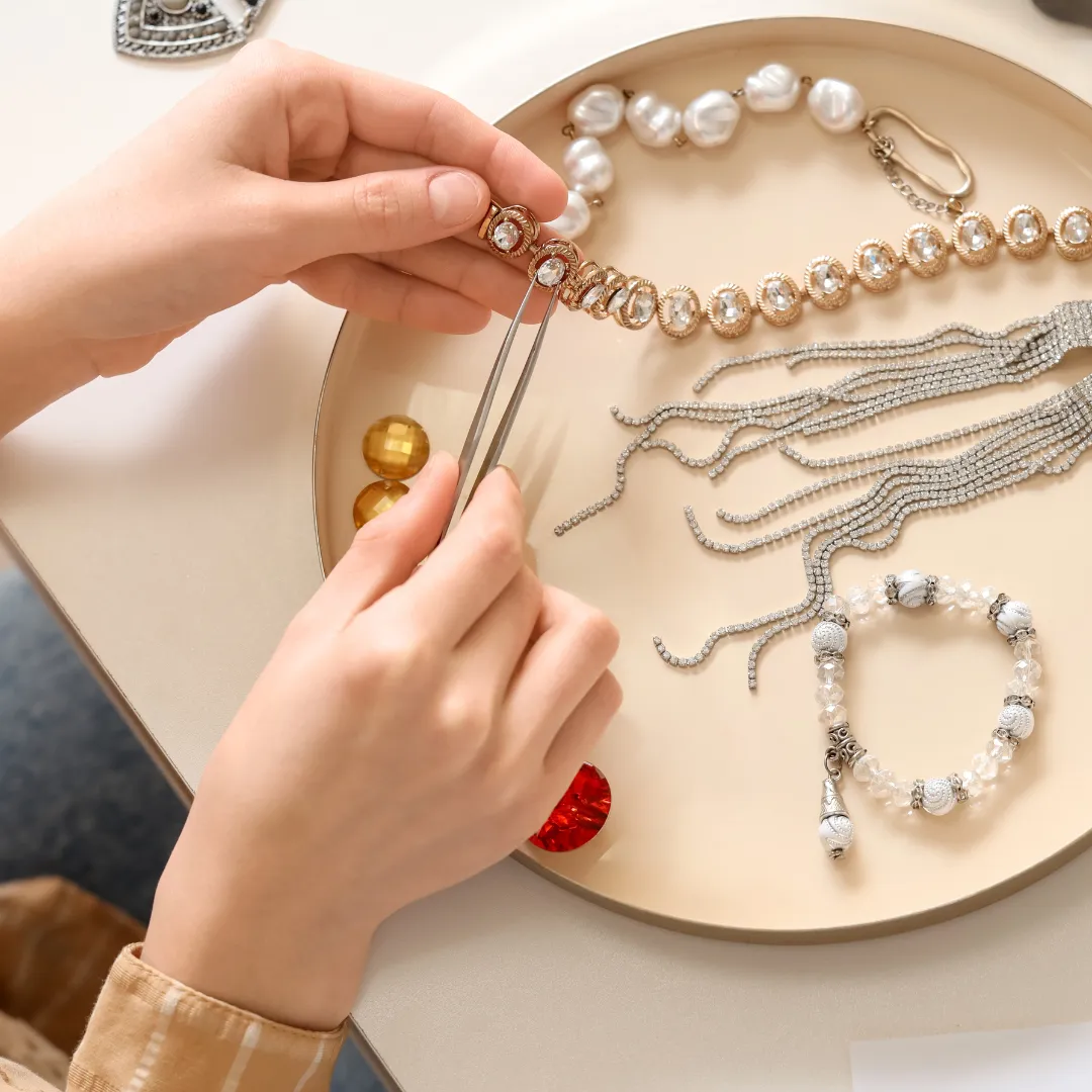 A person using tweezers to arrange jewelry pieces on a tray, showcasing various beads and chains.