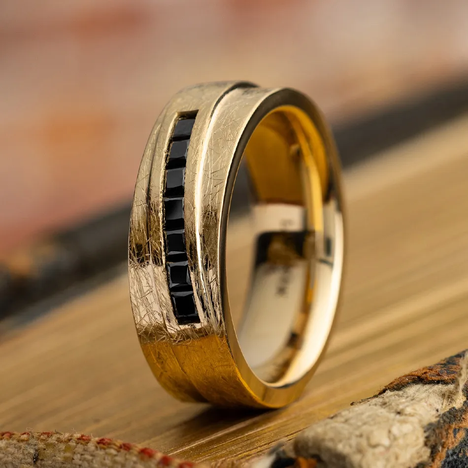 Gold men's wedding band with black stones, showcasing a modern design. Visit Synder Jewelers in Longmont for more.