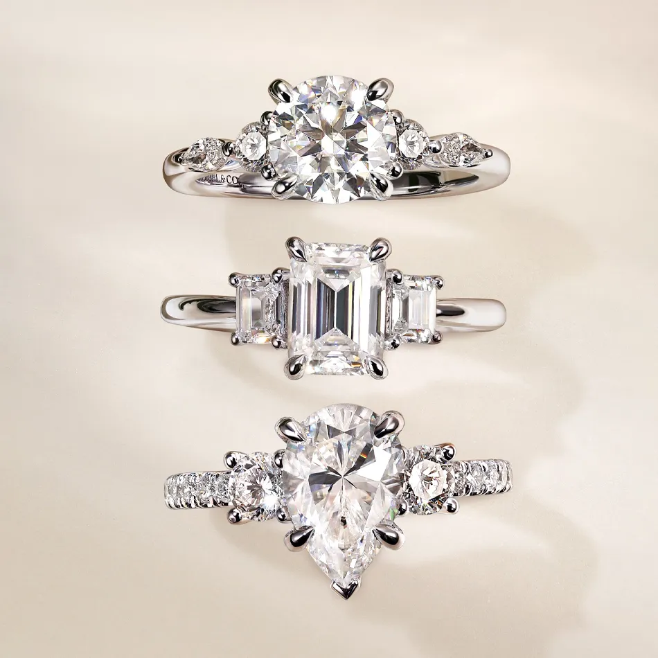 Three elegant engagement rings featuring round, emerald, and pear-shaped diamonds, set in white gold.