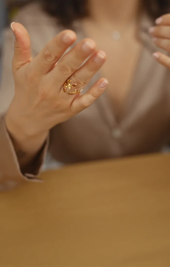 A woman gestures with her hands, showcasing gold and silver rings while wearing a beige blouse. Click to make an appointment.