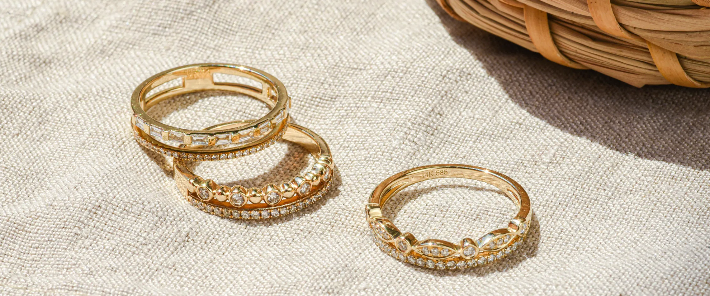 Three elegant gold rings with diamonds displayed on a textured fabric background. Click to start a project at Synder Jewelers.