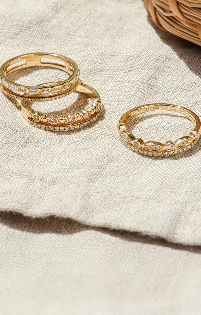 Three elegant gold rings with diamonds displayed on a textured fabric background. Click to start a project at Synder Jewelers.